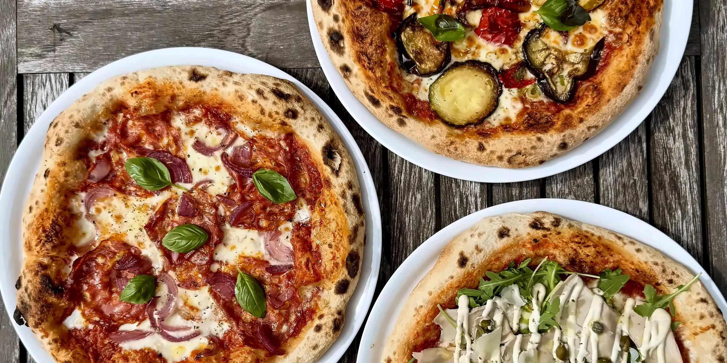 Drei Pizzen auf unseren Böden, belegt nach Karte, auf einem Holztisch